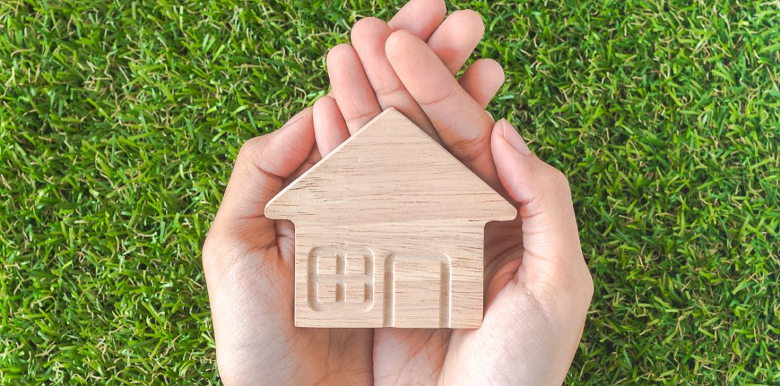 Home shaped on Woman's hand over green grass. Green Home Concept.